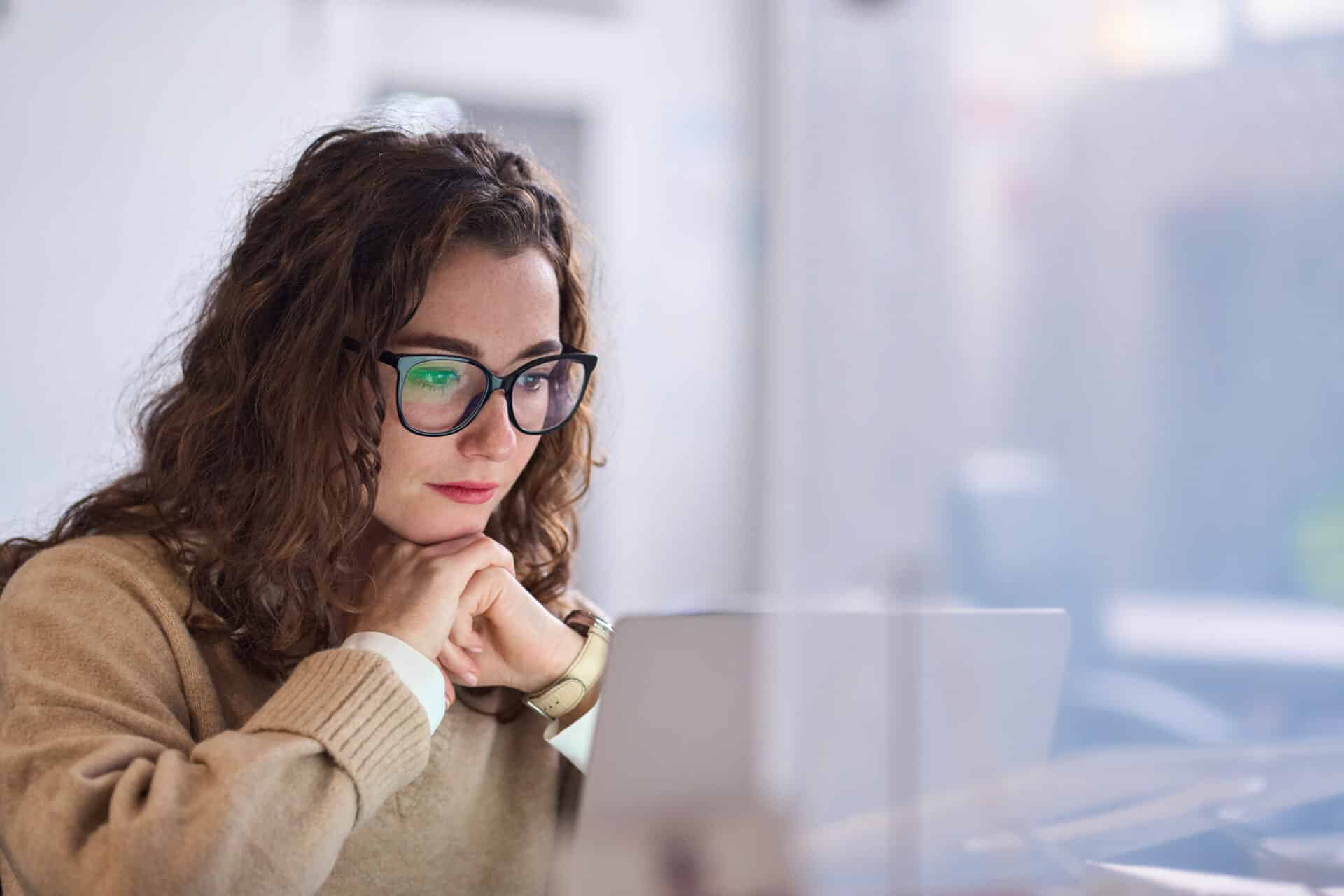 Young woman worker wearing glasses watching online webinar at work.