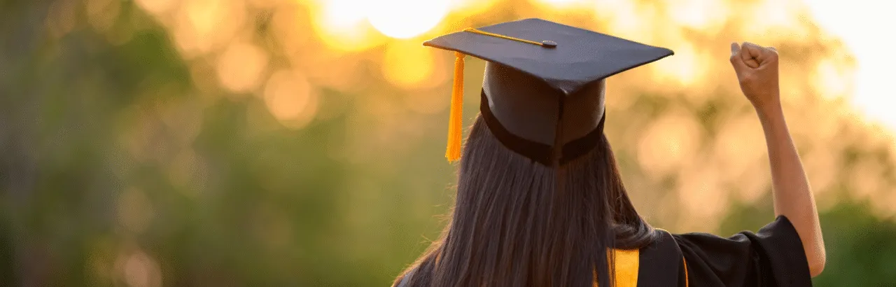 Girl facing away from camera wearing graduate cap and gown holding up right fist