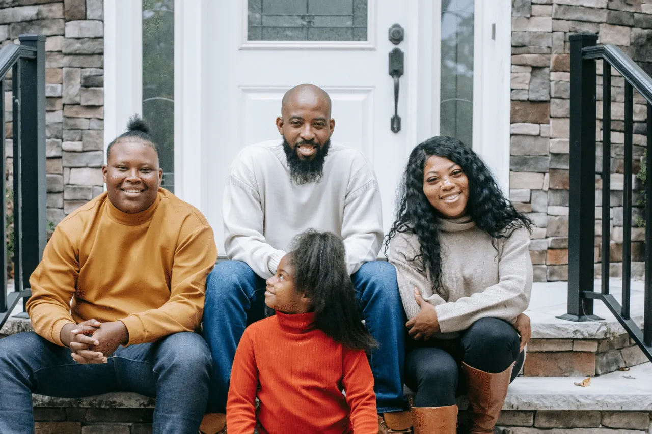 Black family sitting together smiling on steps, young girl looking up at older brother