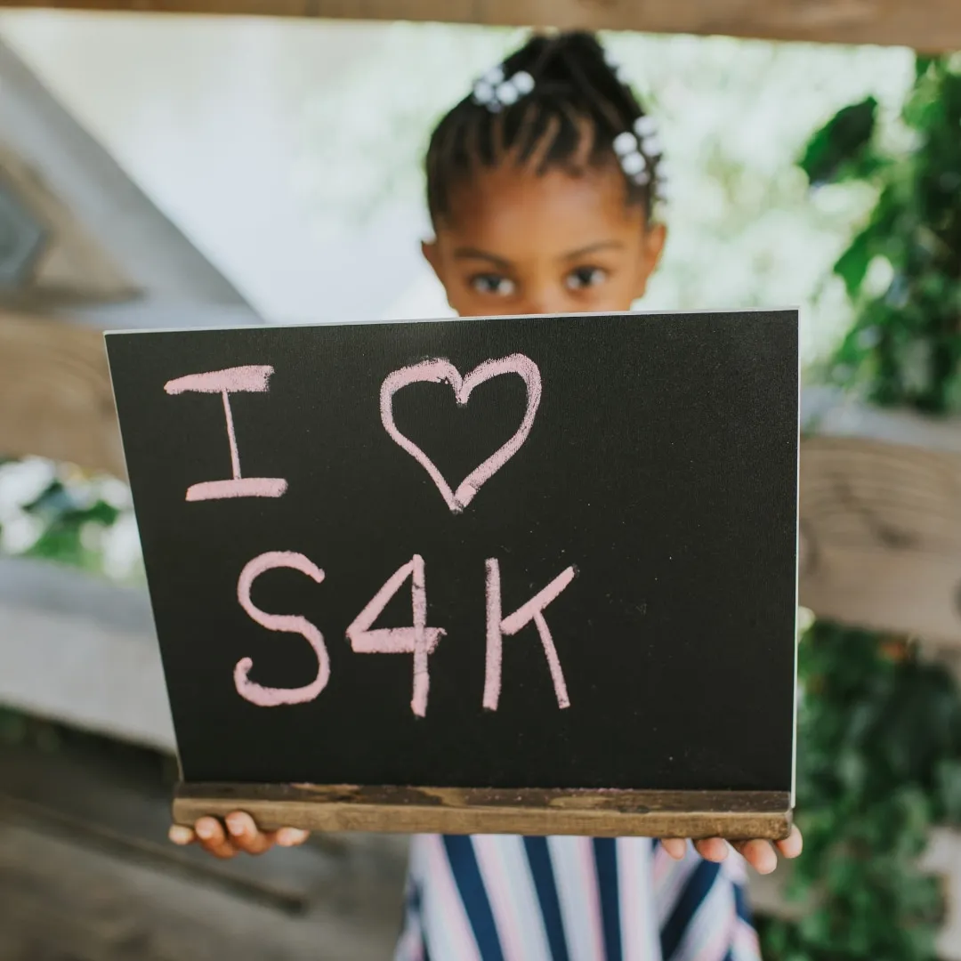 Young girl of color holding I heart S4K chalkboard sign