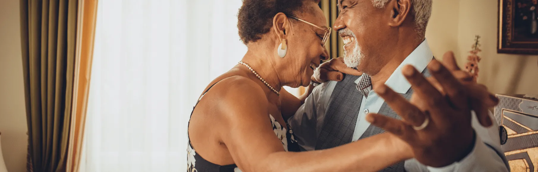 African American wife & husband smiling and dancing in their living room