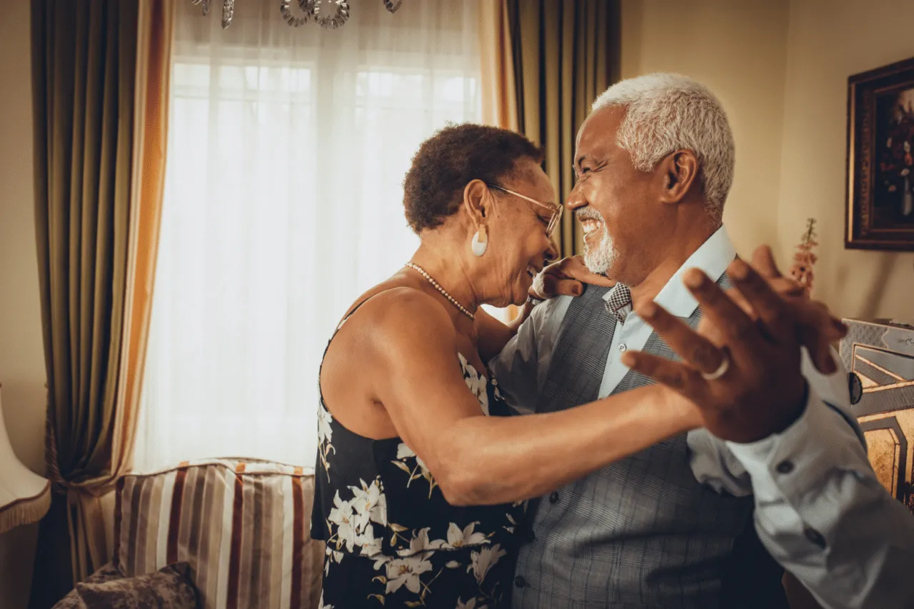 African American wife & husband smiling and dancing in their living room