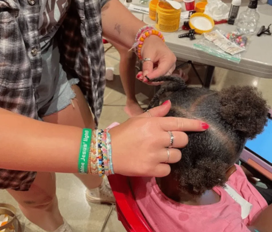 Hair stylist teaching how to part child of color's hair