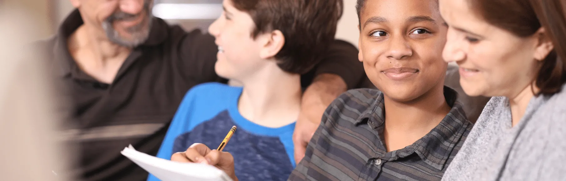 Caucasian adoptive family sitting on couch together, multiracial adoptive son staring at adoptive mother with half smile