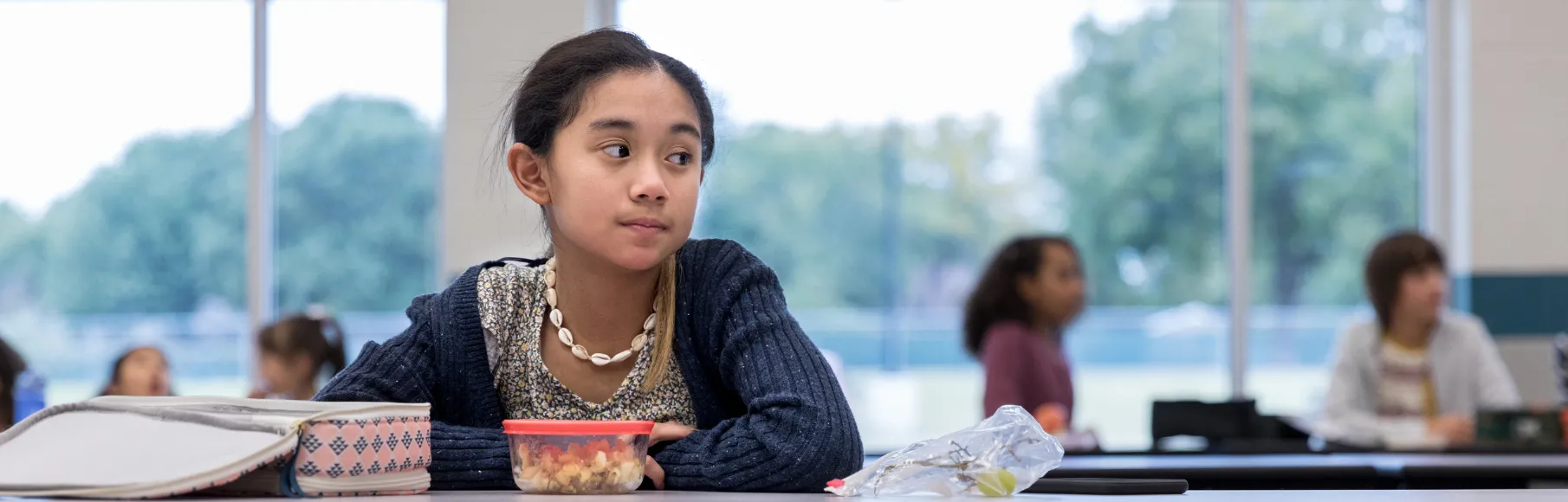 Multiracial teenager sitting at lunch alone looking into distance