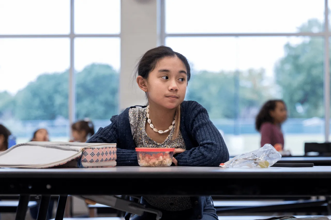 Multiracial teenager sitting at lunch alone looking into distance
