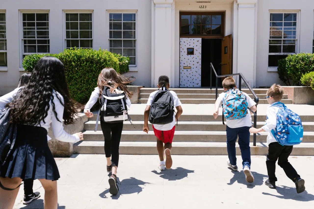 Diverse group of kids wearing backpacks running towards school door