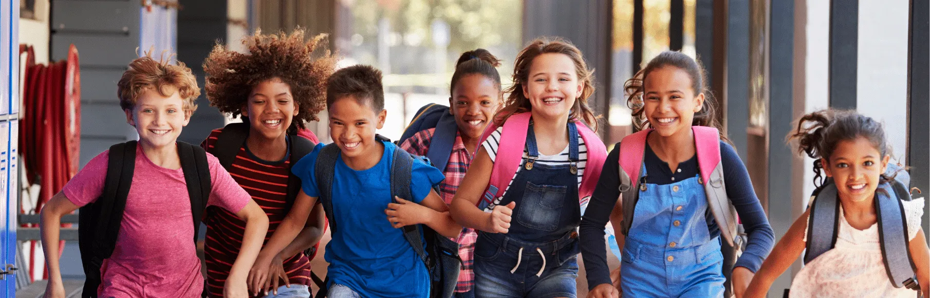 Diverse group of kids smiling and wearing bookbags running down school outdoor hallway