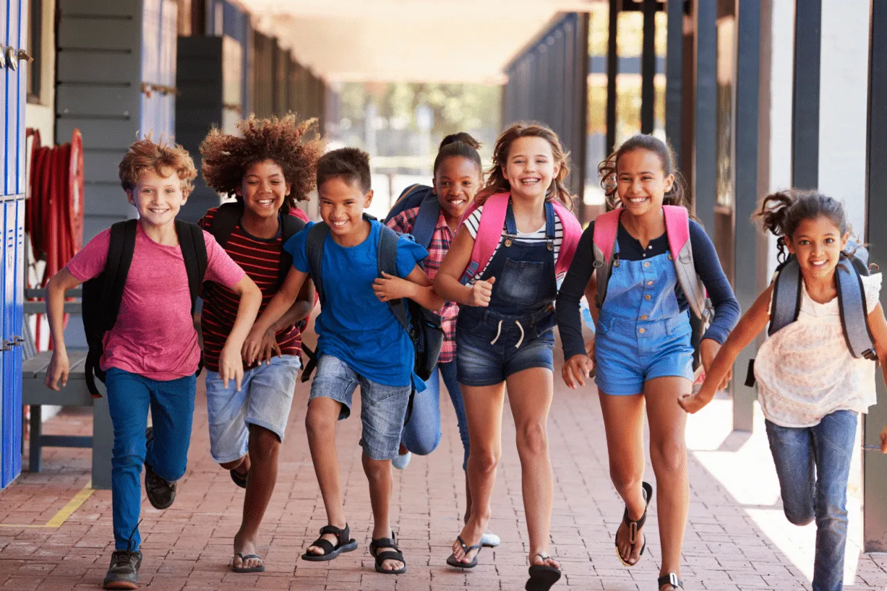 Diverse group of kids smiling and wearing bookbags running down school outdoor hallway