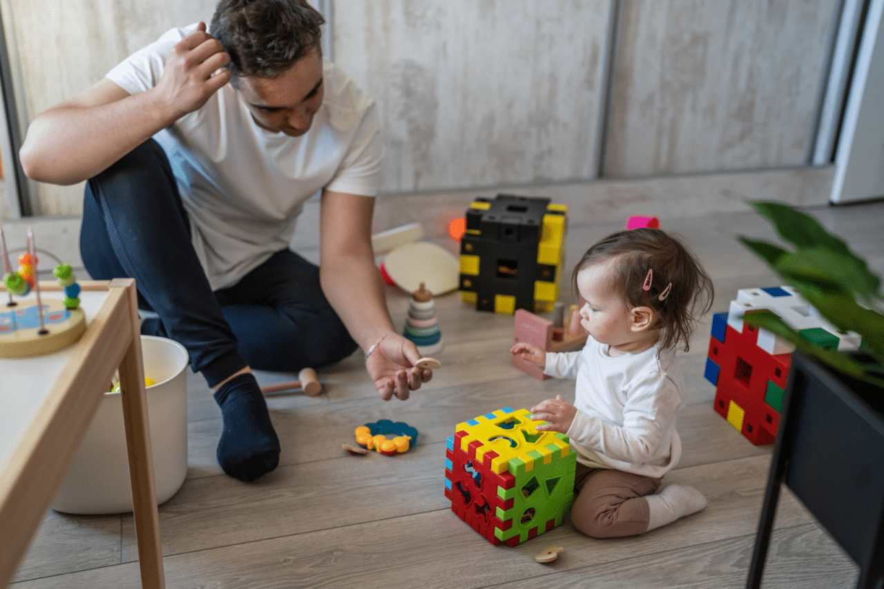 Dad handing young daughter a small wooden toy to hold and play with