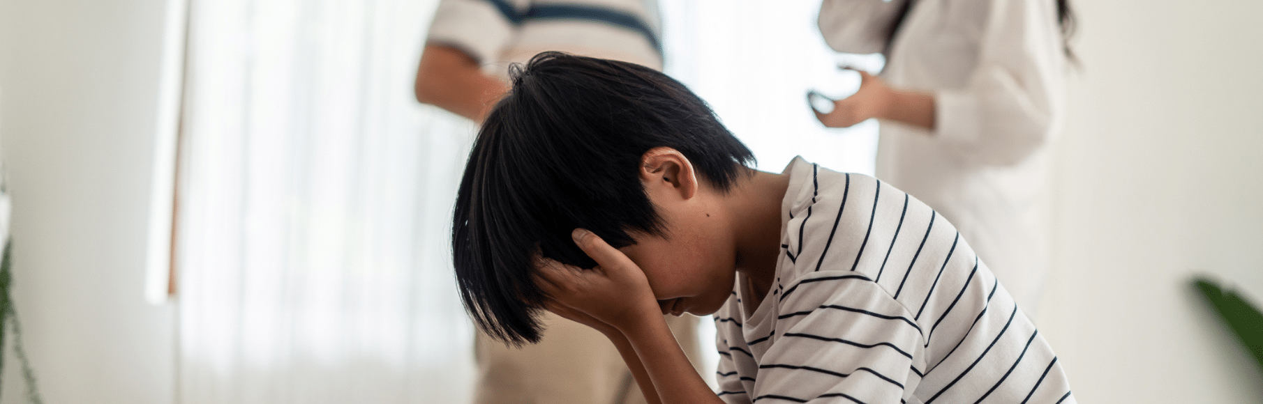 Young boy with head in hands with parents arguing behind him