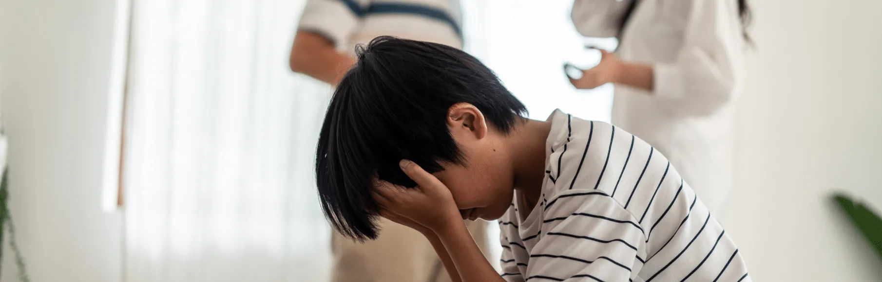 Young boy with head in hands with parents arguing behind him