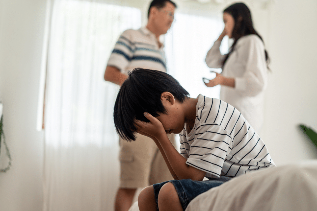 Young boy with head in hands with parents arguing behind him