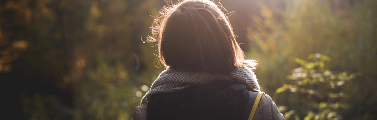 Back of young woman in walking woods with sun glimmer