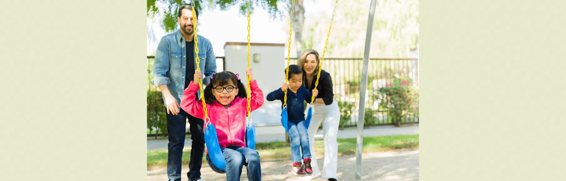 Two young children, boy and girl, swinging with parents pushing them on swing set