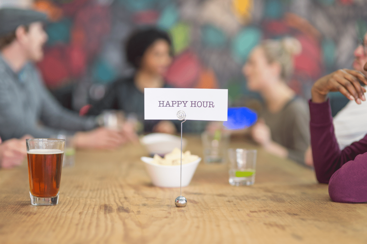 People sitting at table with drinks. Happy Hour sign on table.