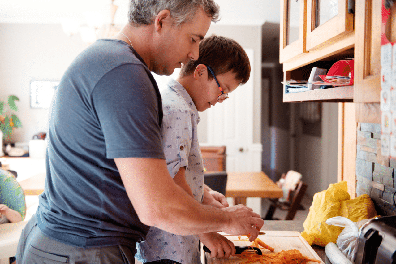 Father helping young son with development differences cut vegetables