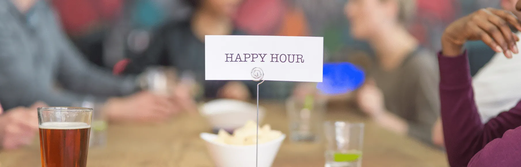 People sitting at table with drinks. Happy Hour sign on table.