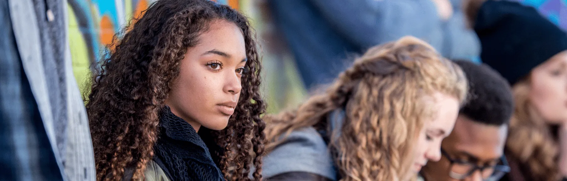 Biracial teen girl serious looking off into the distance surrounded by other teens