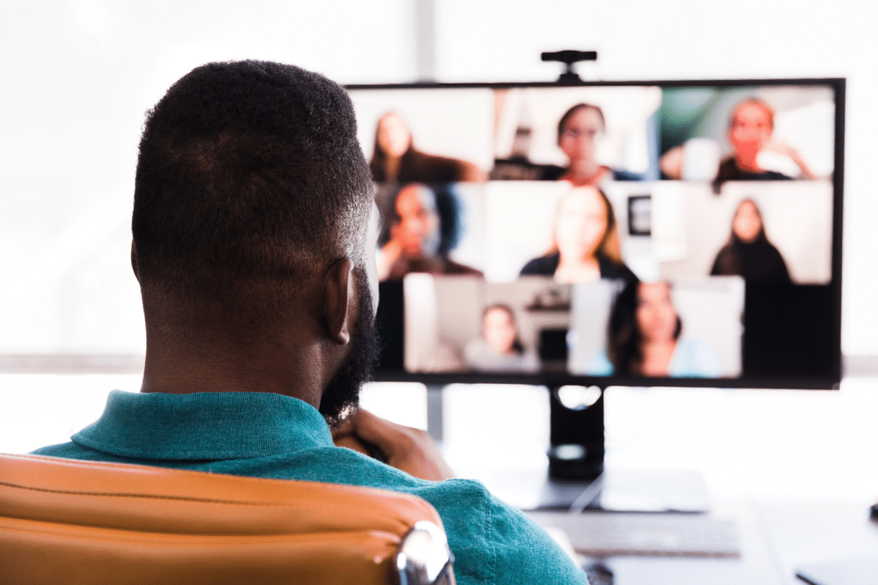 Black man looking at virtual meeting screen on desktop computer, faces blurred on screen