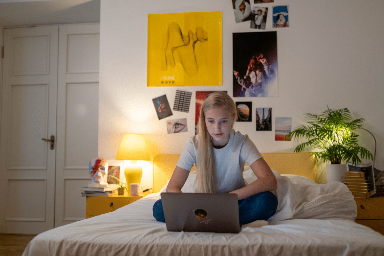 White teen girl sitting on bed looking serious at laptop screen