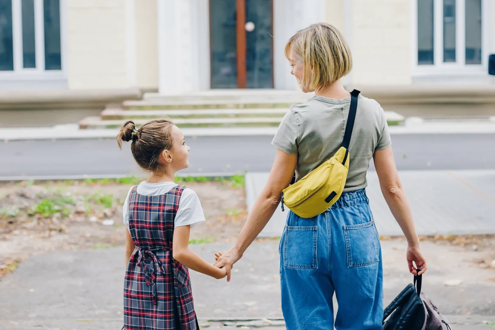 Caucasian mom and young Caucasian daughter holding hands walking into school building