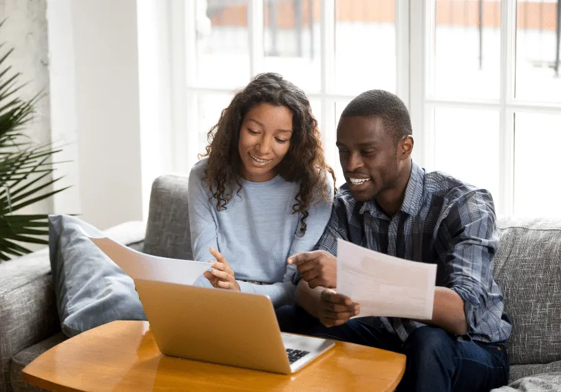 Young black couple smiling looking at papers and laptop