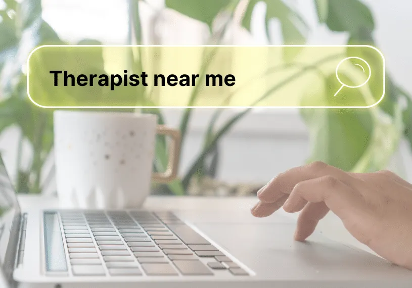 Therapist near me in search bar overlay person using a laptop at desk with cup of coffee