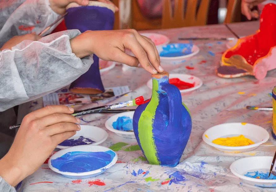 Kid painting piece of pottery blue and green paint