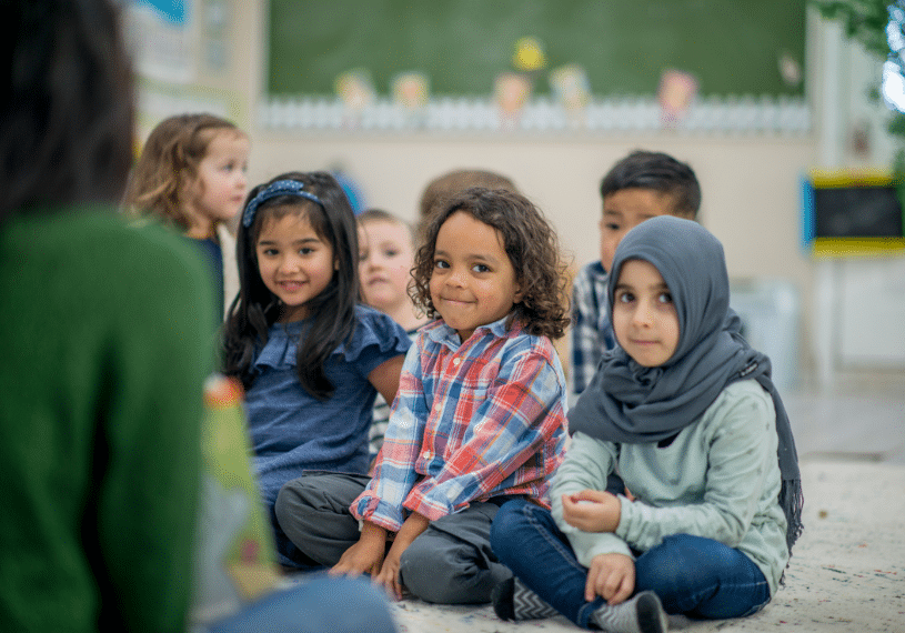 Diverse Group Preschool Children Half smiling sitting on floor in front of teacher