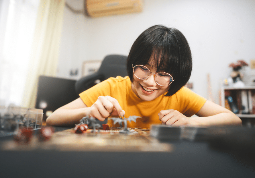 Smiling Asian teen girl wearing glasses playing tabletop game