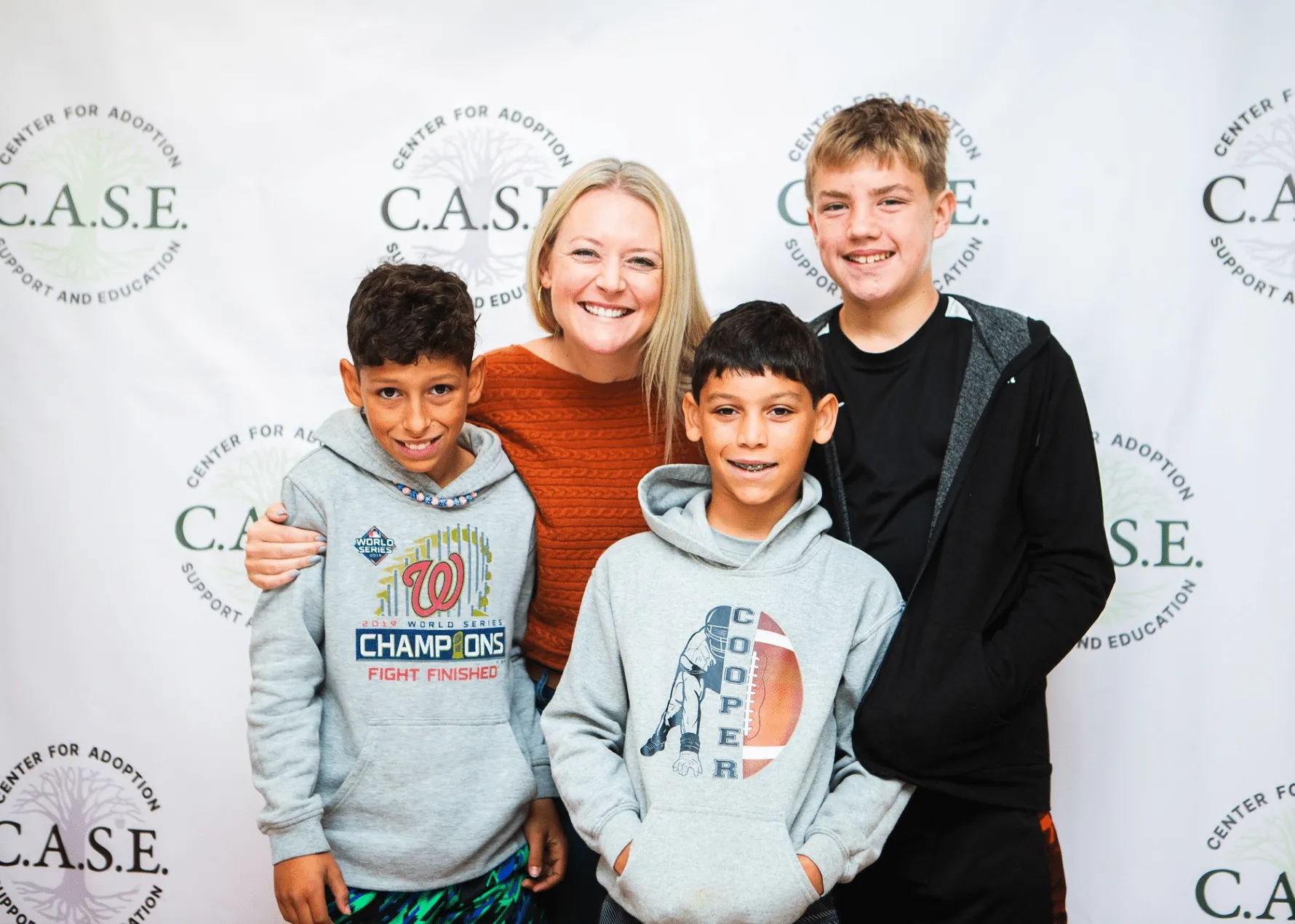 Adoptive Mom and 3 Adoptive Sons Smiling Together in front of C.A.S.E. logo backdrop