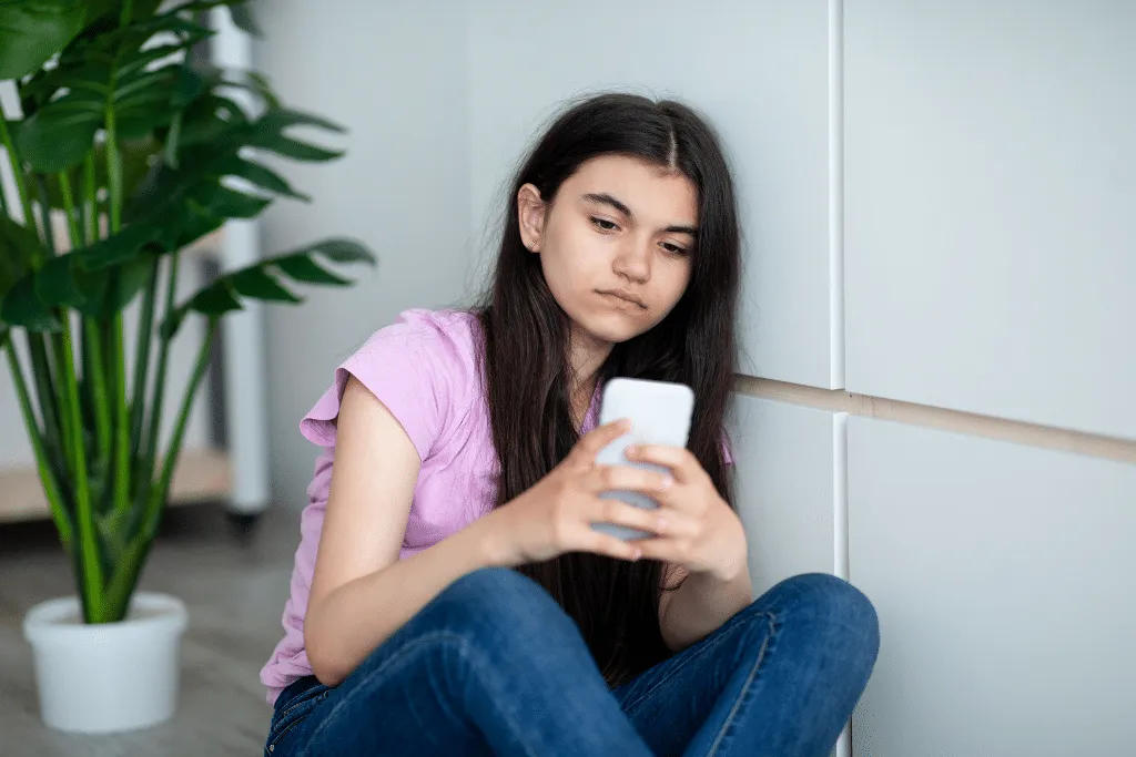 Teenage girl sitting on floor and looking depressed at phone