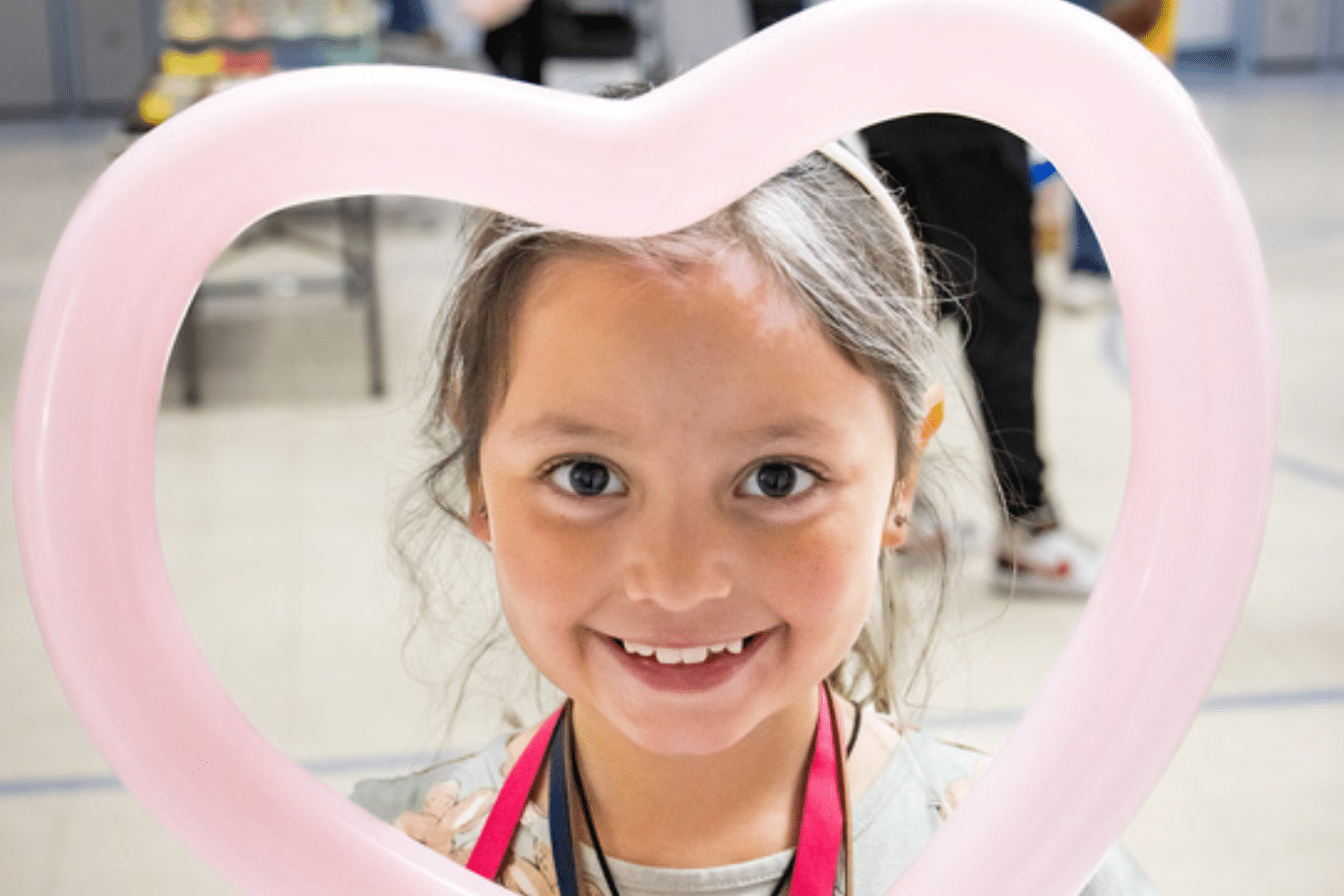 Young girl smiling holding pink heart shaped balloon towards face