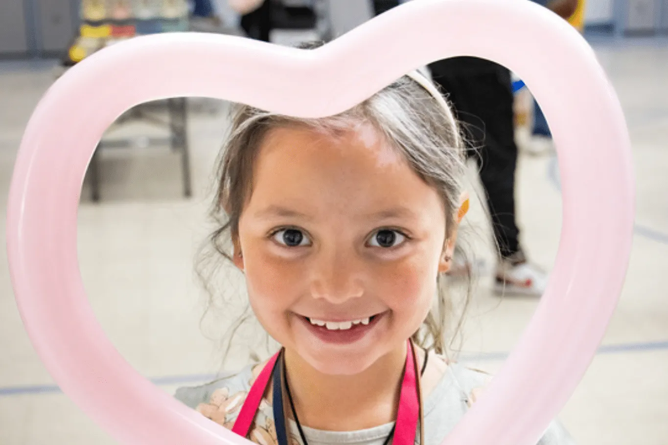 Young girl smiling holding pink heart shaped balloon towards face