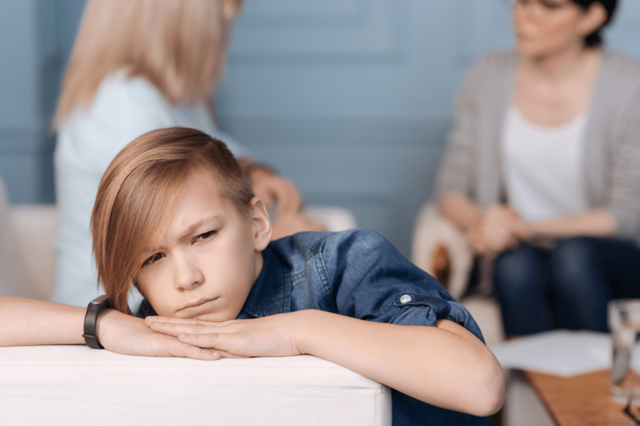 Young boy looking upset while adults talk in the background